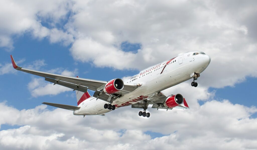 White and red airplane flying in the air under clouds